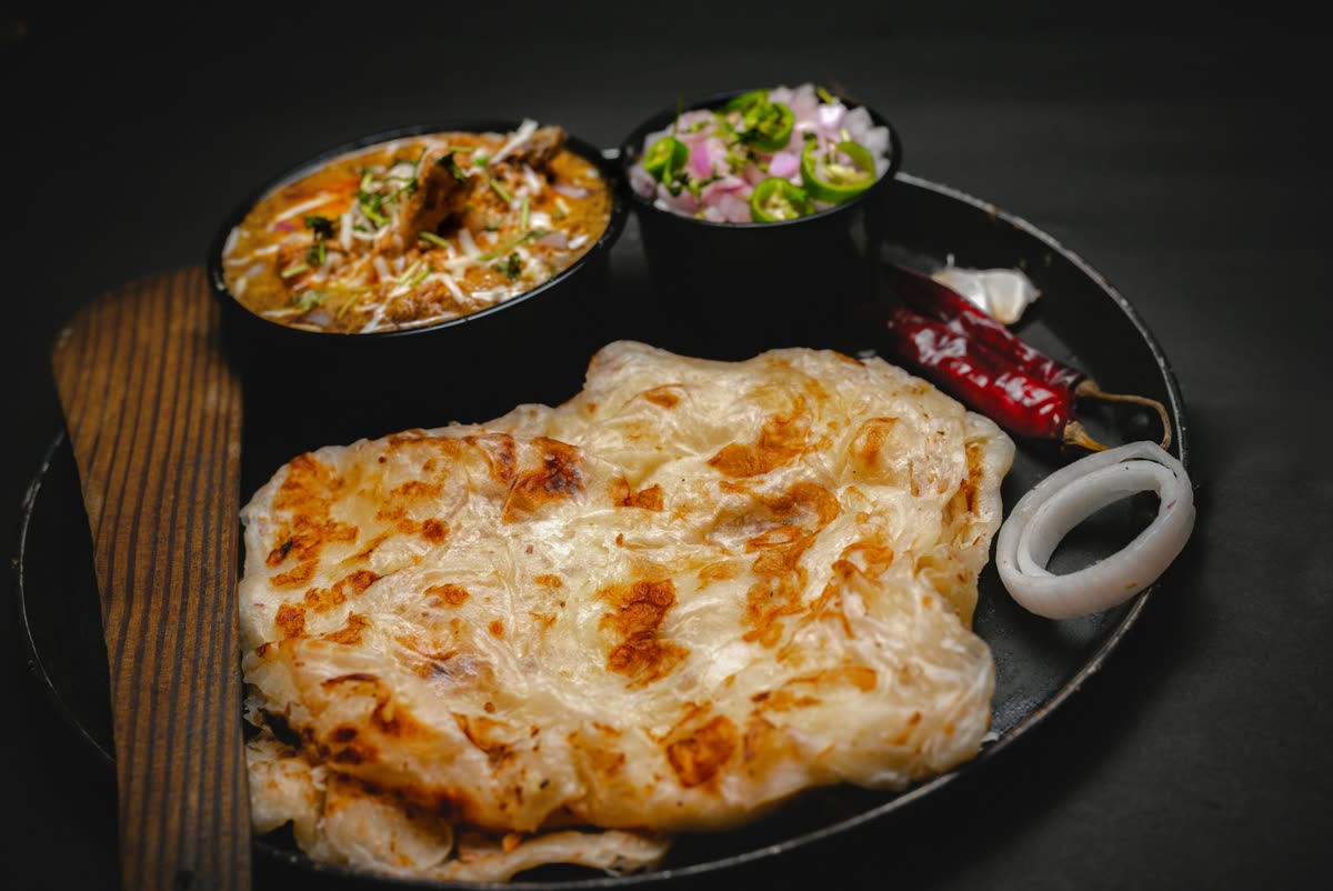 Flaky roti served with a bowl of curry and sliced onion